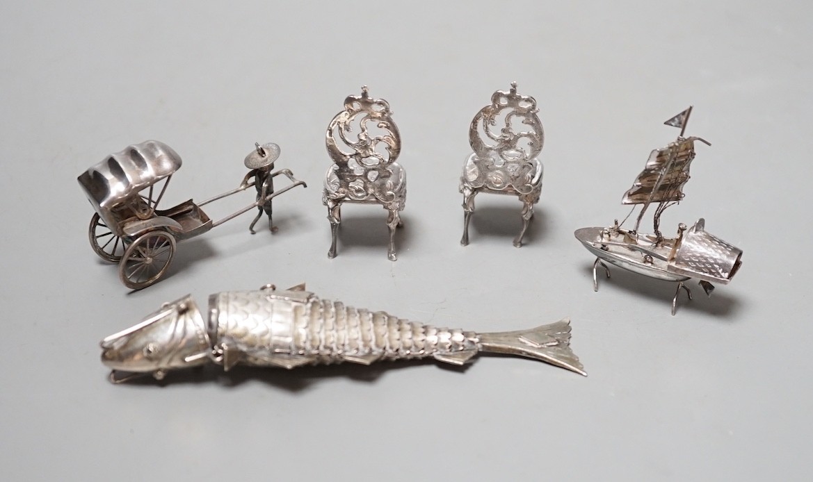 A pair of miniature white metal occasional chairs, a sterling rickshaw and boat and an articulated fish pill box.